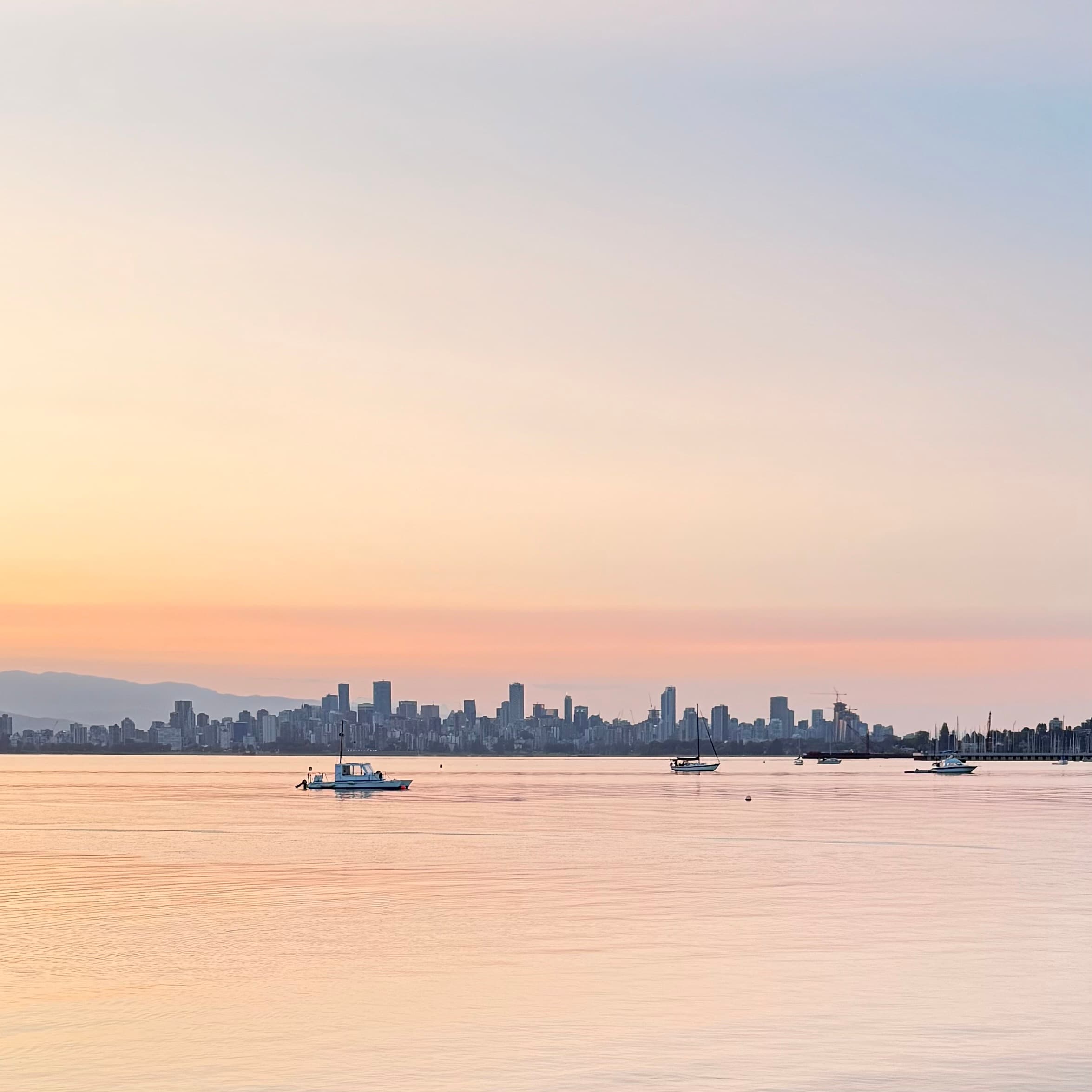 Pink and orange sunrise over English Bay, Vancouver skyline silhouette reflected in calm water, race morning of T100 Vancouver 2025