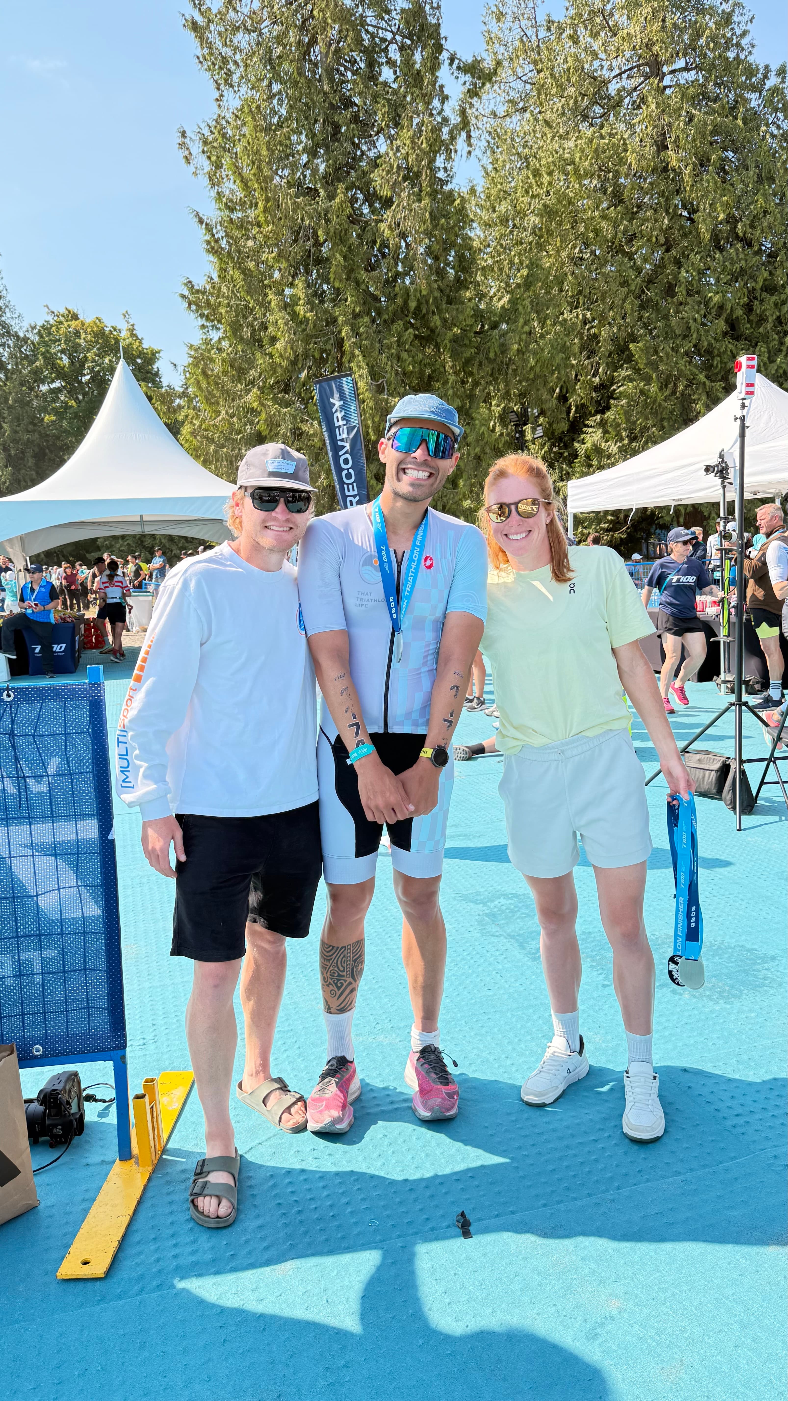 Lucas Calegari with Eric Lagerstrom and Paula Findlay at the T100 Vancouver 2025 finish line, wearing the TTL triathlon kit with finisher medal