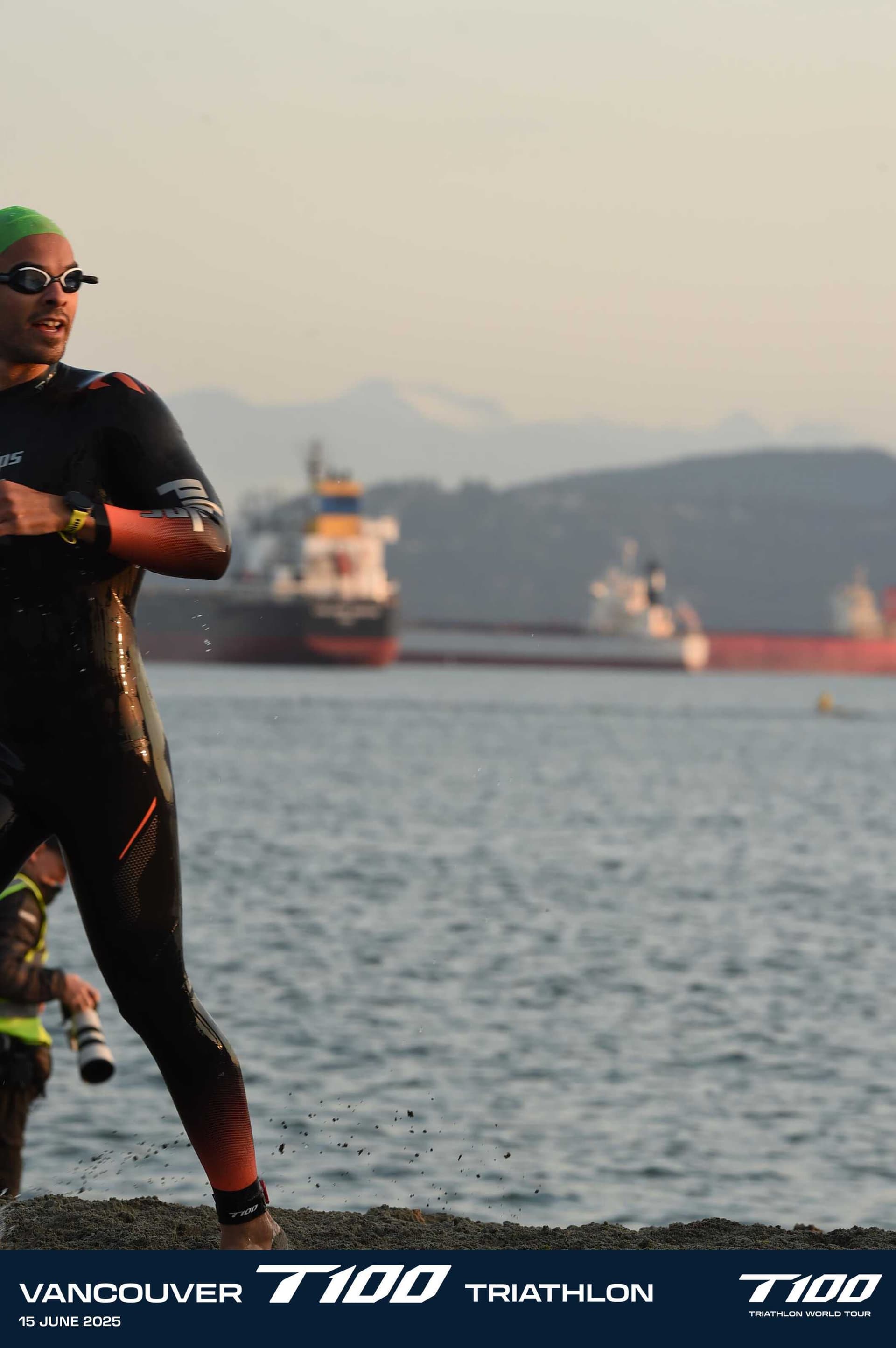 Lucas Calegari exiting the water at T100 Vancouver 2025, Vancouver skyline and cargo ships in the background at sunrise