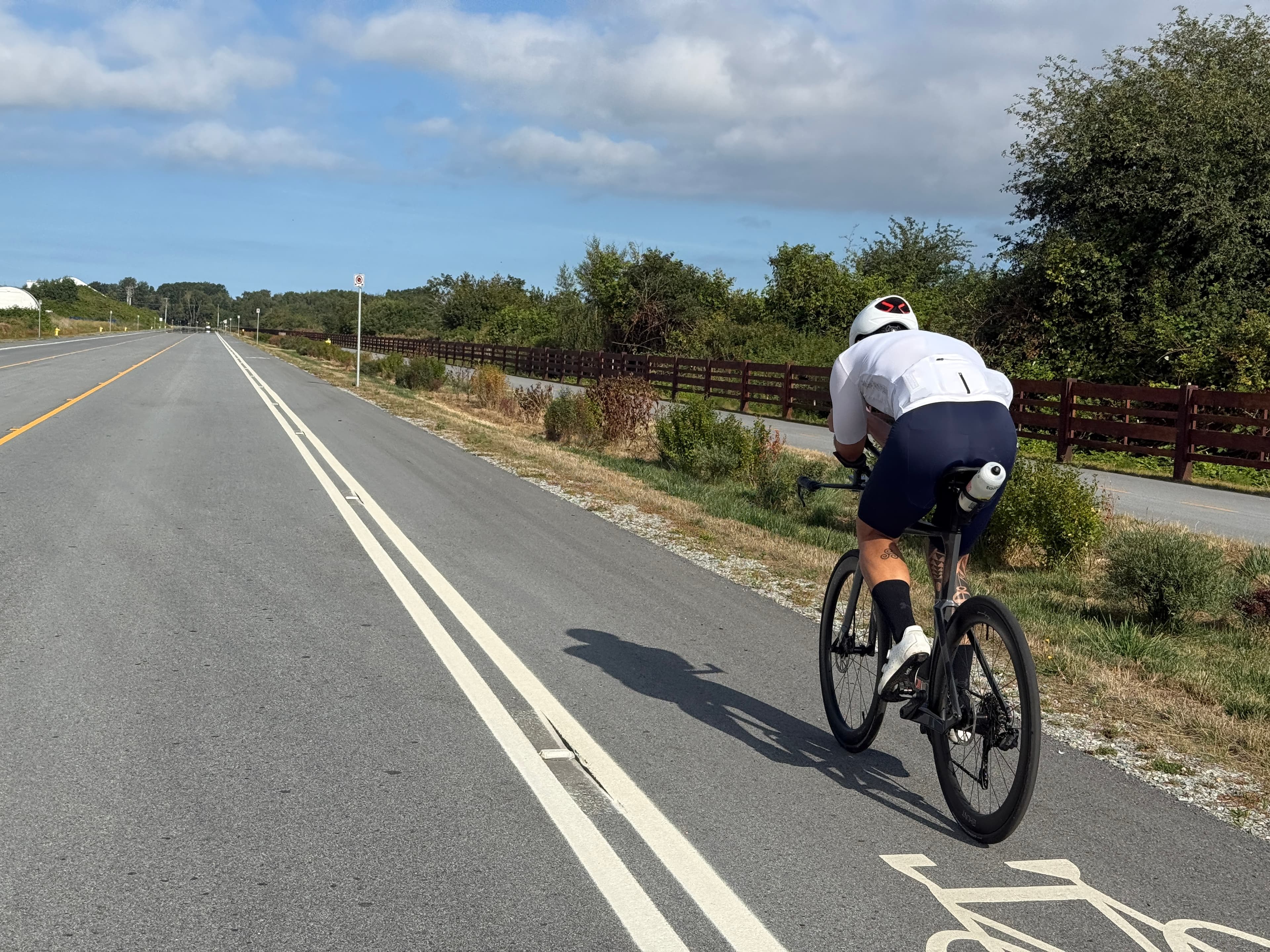 Lucas Calegari in aero position on his triathlon bike during the Sunday long ride, riding a bike path lined with wooden fencing and trees