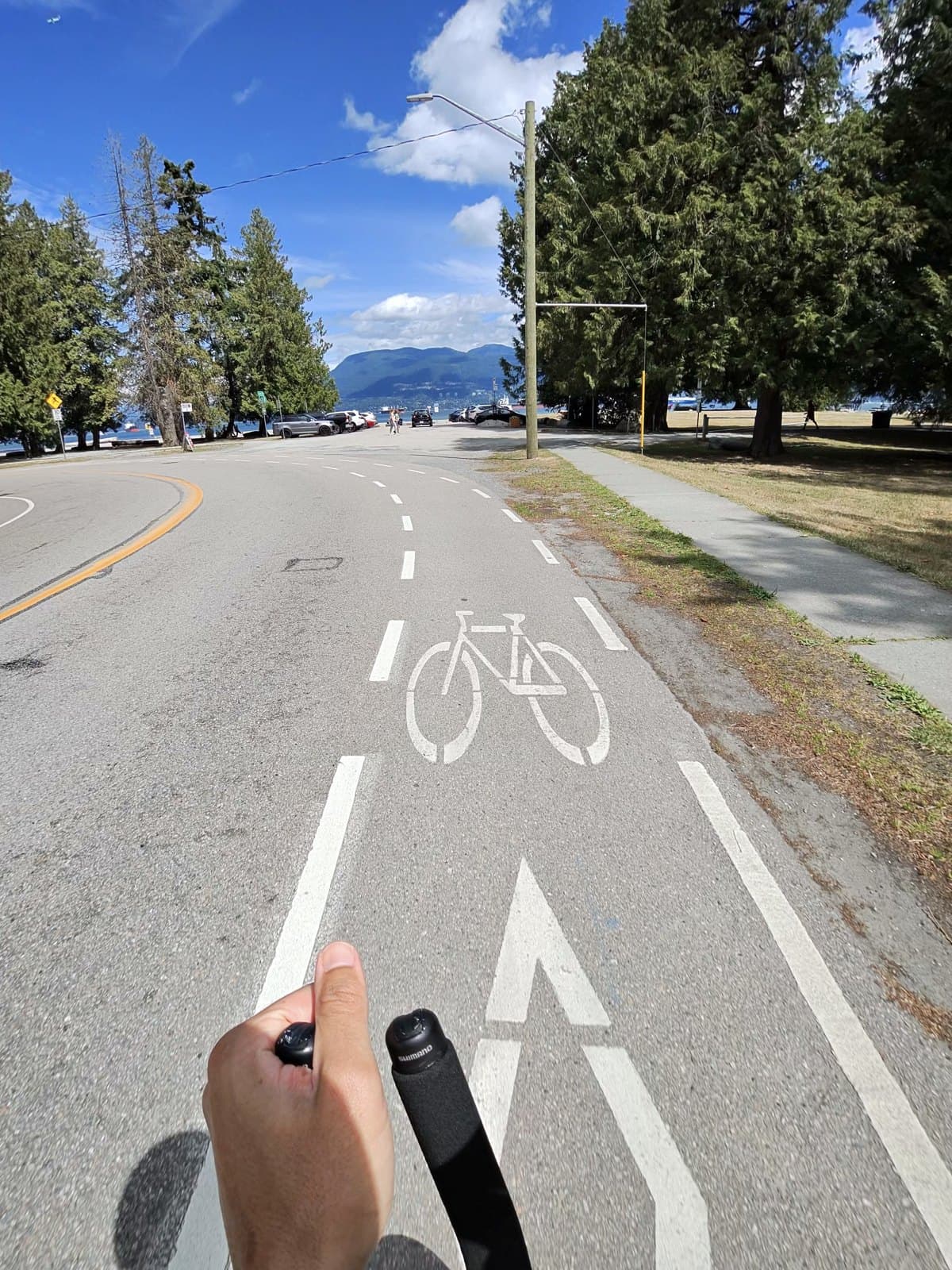 POV from the aerobars on the Stanley Park seawall bike lane, painted bike symbol on the road, English Bay and the North Shore mountains under a clear blue sky
