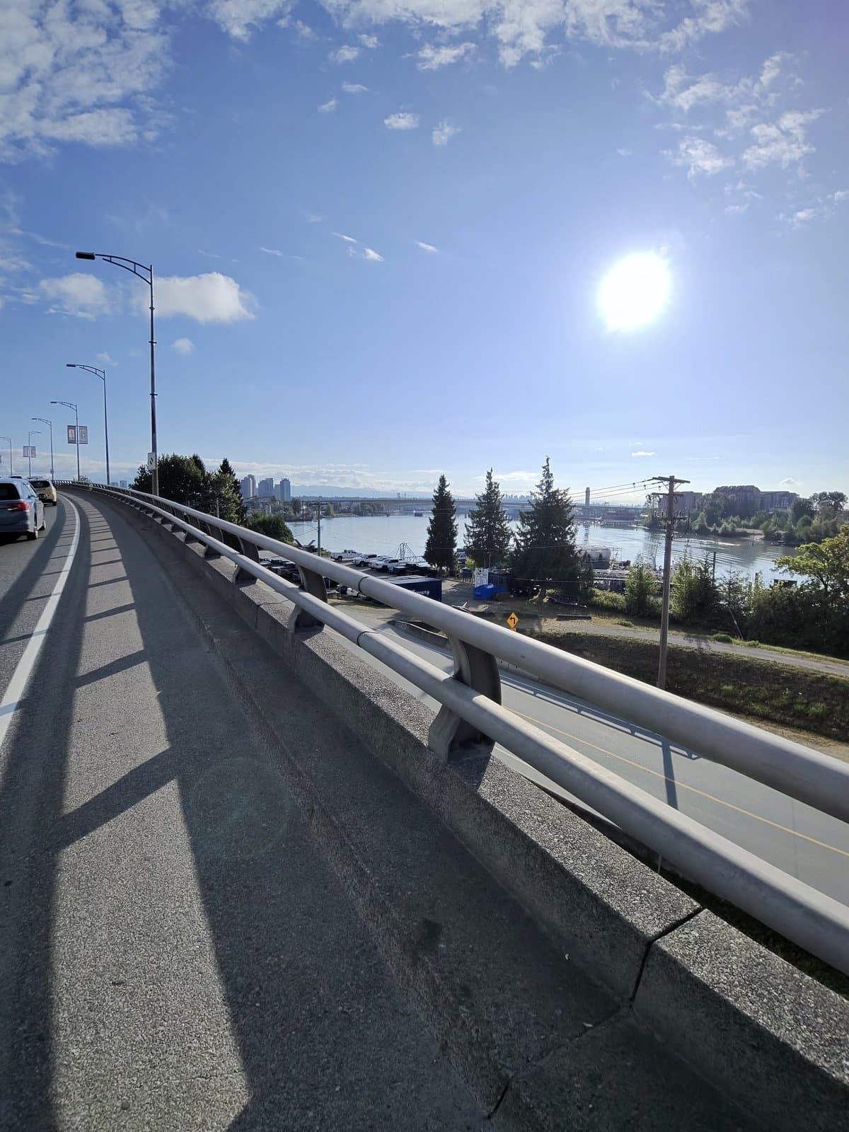 Sunday morning ride crossing a bridge, guardrail running along the shoulder, the river and distant city towers below a clear blue sky with the sun high and bright